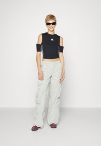 Μαύρο cropped top με κοψίματα στους ώμους και λευκό λογότυπο, σε συνδυασμό με ανοιχτό γκρι cargo παντελόνι με πλαϊνές τσέπες και χαλαρή εφαρμογή.