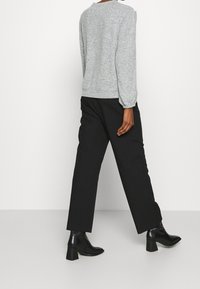Šedý vzorovaný svetr s kulatým výstřihem, kombinovaný s černými volnými kalhotami a černými kotníkovými botami s robustním podpatkem.