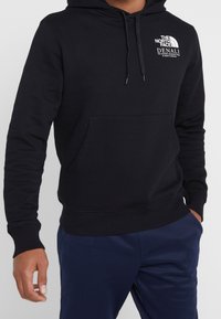 Felpa nera con cappuccio, tasca frontale, polsi e orlo a costine, con il logo "The North Face Denali" in bianco sul petto.