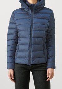 Giacca trapuntata blu navy con zip frontale, design trapuntato orizzontale e cappuccio. Dotata di tasche laterali e polsini elasticizzati per garantire comfort.