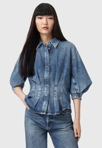 Giacca di jeans blu chiaro con chiusura a bottoni, maniche oversized e tasche laterali. Presenta una vestibilità su misura e una trama sbiadita.