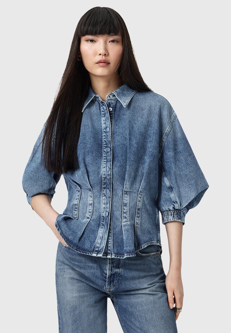 Giacca di jeans blu chiaro con chiusura a bottoni, maniche oversized e tasche laterali. Presenta una vestibilità su misura e una trama sbiadita.