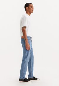 Lyseblå denimjeans med rett passform, kombinert med en enkel hvit t-skjorte og svarte sneakers. Har baklommer og synlige sømmer.