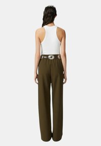 Top bianco senza maniche abbinato a pantaloni olive verdi a vita alta e a gamba larga. I pantaloni presentano una cintura testurizzata con dettagli argentati.
