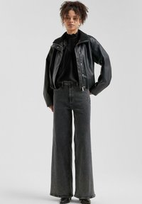 Giacca in pelle nera cropped su una blusa nera con scollo arricciato, abbinata a jeans in denim grigio a gamba larga a vita alta.