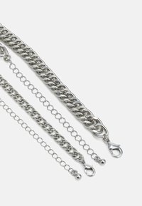 Colar de corrente de metal prateado com três designs de elos diferentes. Apresenta um fecho tipo lagosta e uma textura lisa e brilhante.