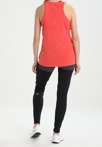 Röd, ärmlös sporttopp med strukturerad yta, kombinerad med tapered svarta byxor som har sidofickor och en figurnära passform.