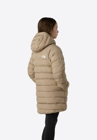 Beež värvi puffer-jakk, millel on kitsenev kapuuts, vertikaalne triibustus, The North Face'i logo vasakul õlal ja keskmise pikkusega lõige.