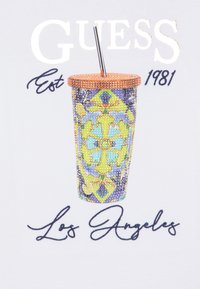 Gráfico de una colorida taza joya con una tapa marrón, que presenta diseños intrincados en azul, verde y amarillo, junto con el texto "GUESS Est 1981 Los Ángeles."