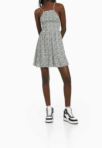 Black and white floral print dress with a fitted bodice, flared skirt, and thin straps. Paired with black and white high-top sneakers.