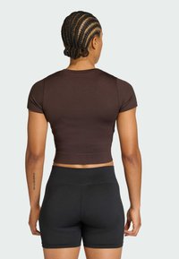 Καφέ crop top με κοντά μανίκια, συνδυασμένο με μαύρα σορτς ψηλόμεσα που διαθέτουν υφή και λείο φινίρισμα.
