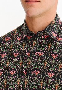 Czarna koszula w kwiaty z różowymi i zielonymi roślinnymi wzorami, krótki kołnierz i guziki, wykonana z lekkiego materiału.