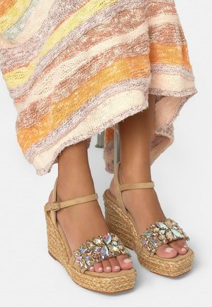 Beige sleehak sandalen met enkelbandjes en multicolor edelsteenversieringen, gedragen met een multicolor gestreepte gebreide rok.