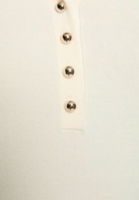 Tessuto a coste di colore crema chiaro con cinque bottoni metallici lungo la pettorina. Texture liscia con un design aderente, che presenta una leggera lucentezza.