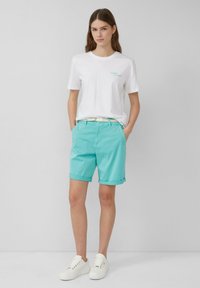 Witte katoenen t-shirt met minimale tekst, gecombineerd met lichtblauwe shorts met opgerolde hems en een geweven riem, afgemaakt met witte sneakers.