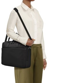 Bolso de hombro de tela negra con asas dobles, una correa desmontable y un bolsillo frontal con cremallera. Textura suave y forma rectangular.