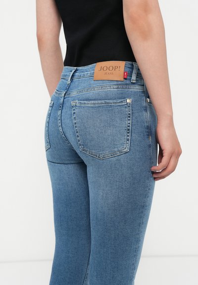 Jean en denim bleu clair avec une coupe ajustée. Présente une étiquette en cuir portant la mention "JOOP! JEANS" à la taille, ainsi que deux poches arrière avec des coutures.