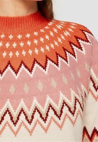 Gebreide trui met een hoge halslijn, versierd met een geometrisch patroon in rood, oranje, roze en crème kleuren; gladde textuur met zigzag accenten.