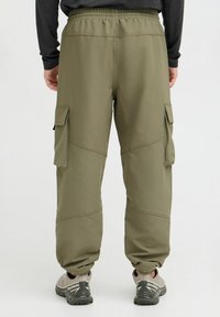 Pantalones cargo oliva con cintura elástica, bolsillos laterales y detalles cosidos, combinados con zapatillas deportivas grises. Textura mate.