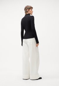 Pull à col roulé noir à côtes avec des manches longues, associé à un pantalon blanc ample. Le pantalon a des bas de pantalon larges et des poches arrière.
