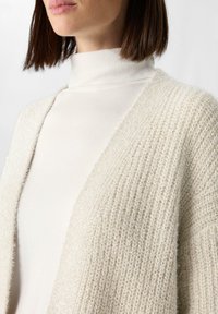Lichtbeige cardigan van textuur gebreide stof, met een ontspannen pasvorm en geribde accenten bij de kraag en manchetten.