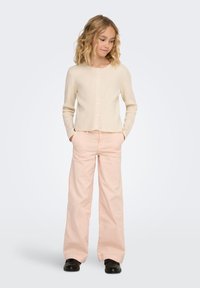Light beige ribbed cardigan with round neckline and button closure, paired with loose, pale pink trousers and black shoes.