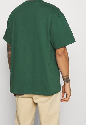 T-shirt en coton vert avec une coupe décontractée, des manches courtes, un col rond et une texture lisse. Présente des coutures le long de l'ourlet et des manches.