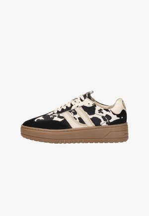 Black and white cow-print sneaker with a beige suede stripe, round toe, and brown rubber sole. Features white laces and a textured finish.