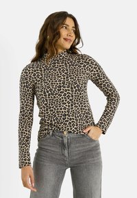 Haut à manches longues imprimé léopard en beige et noir, avec un col montant et une coupe ajustée. Associé à un jean gris taille haute.