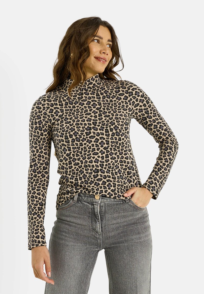 Haut à manches longues imprimé léopard en beige et noir, avec un col montant et une coupe ajustée. Associé à un jean gris taille haute.