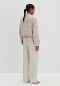 Beiger, strukturierter, kürzer geschnittener Blazer mit Falten, langen Ärmeln und hochgeschlossenem Kragen, kombiniert mit hoch taillierten, cremefarbenen, weit geschnittenen Hosen.