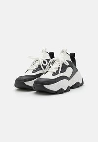 Kraftige svart-hvite sneakers med mesh-overdel, gummisåle og kontrasterende glatte skinndetaljer. Inkluderer hvite snørebånd og pull-tabs.
