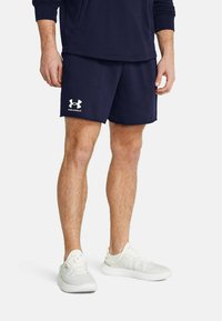 Mörkblåa träningsshorts med en slät textur och vit Under Armour-logga. Kombinerade med ljusfärgade sportskor med nätdesign.