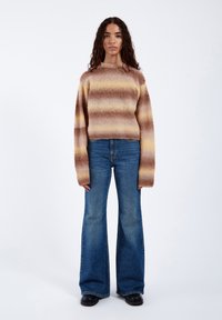 Strickpullover mit horizontalen Streifen in Brauntönen und Creme, langen Ärmeln und Rundhalsausschnitt, kombiniert mit ausgestellten blauen Jeans.