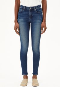 Jeans en denim bleu taille haute, ajustés, avec une légère décoloration, un design à cinq poches et une texture lisse. Ourlet à la longueur de la cheville.