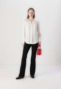 Blusa di cremoso leggera con scollatura arricciata, pantaloni neri aderenti e una piccola borsa rossa. Scarpe col tacco nere completano il look.