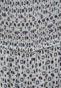 Blauwe en witte jurk met patroon, met een gesmokte lijfje met verhogingen in de textuur, en een uitlopende rok versierd met een luipaardprint.