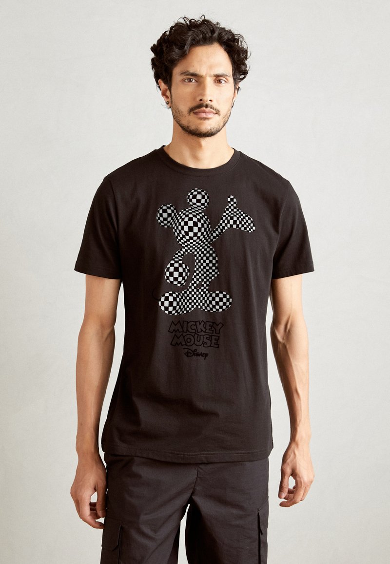 Camiseta de algodón negra con un gráfico de Mickey Mouse en cuadros en blanco y gris, con el texto "Mickey Mouse" debajo en negro. Manga corta, cuello redondo.