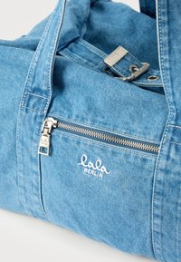 Τσάντα χειρός από ανοιχτό μπλε τζιν με ασημένια τσέπη με φερμουάρ και κεντημένο λογότυπο "lala BERLIN" σε λευκό στο μπροστινό πάνελ.