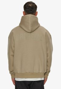Beige hættetrøje med en stor hætte og ribbede manchetter. Teksten "DROPSIZE" præsenteret i ryggen. Blødt stof, afslappet oversized pasform.