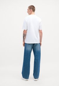 T-shirt in cotone bianco indossato con jeans di denim leggeri di un blu chiaro, caratterizzati da una finitura sbiadita e una silhouette a gamba dritta.