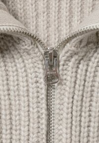 Strickpullover in Hellgrau mit strukturiertem, geripptem Design. Verfügt über einen silbernen Reißverschluss und einen mit Stoff gefütterten Kragenöffnungs für zusätzlichen Komfort.