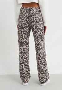 Calças largas com padrão de leopardo, apresentando uma cintura alta, bolsos traseiros, uma textura suave e um corte descontraído, com uma cor base clara e manchas escuras.