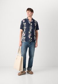 Mornarsko cvetlični kratkotrajni shirt, jeans hlače, bež torba in rjave sandale. Ima barvit cvetlični vzorec na lahkem materialu.