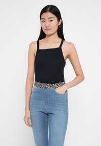 Must rinnahoidjaga topp ruudukujulise kaelusega ja kitsaste rihmadega, kombineeritud kõrge vöökohaga helesiniste teksadega, millel on leopardimustriga vöökoht.