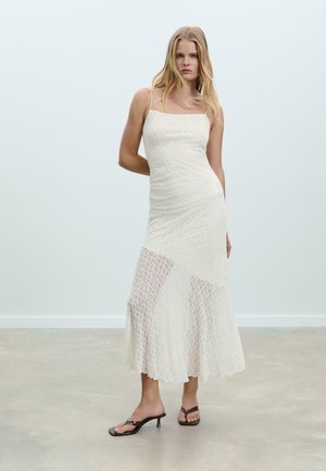 White, fitted dress with a textured, knitted design. Features thin straps, a flared hem, and cut-out accents at the lower section.