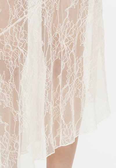 Υφασμα από λευκή δαντέλα με λουλουδένια και γεωμετρικά μοτίβα, σχηματίζοντας διαφανή υφή και λεπτομέρειες από ευαίσθητη κεντητική, που πέφτει πάνω σε πόδι.