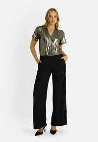 Haut argent métallique à manches courtes avec un décolleté en V profond associé à un pantalon noir à jambes larges. Le pantalon est en tissu texturé et dispose de poches latérales.