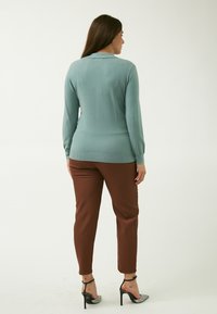 Maglione azzurro chiaro con orlo a coste, abbinato a pantaloni marroni su misura. L'outfit presenta scarpe con tacco alto con un accento scintillante.