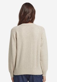 Beige stickad tröja med rundad halsringning, ribbad nederkant och ärmslut, med avslappnad passform och slät textur. Bakvy visas.